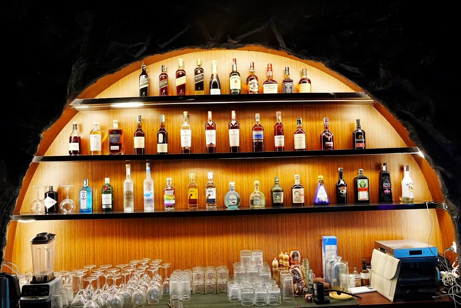 Rows of bottles on lit amber shelves inside a rock arch