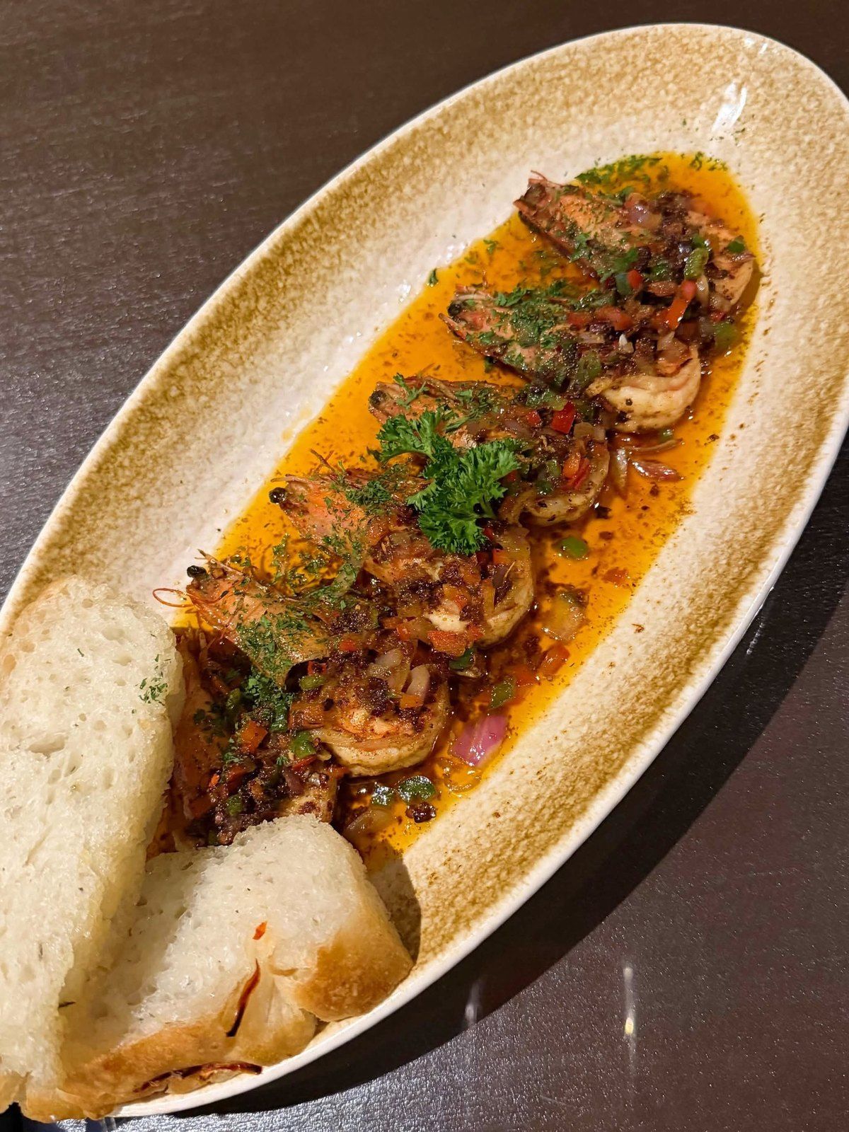 Shrimp in a rich orange sauce in a long speckled dish, with slices of bread
