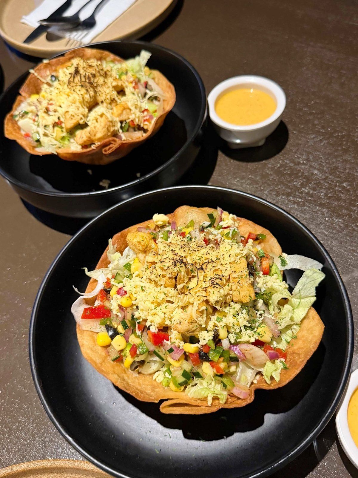 Two crisp tortilla bowls filled with salad, with a small dipping sauce