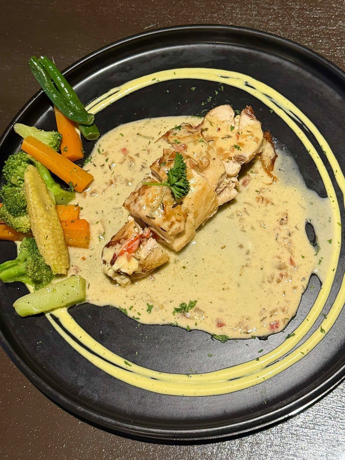 Sliced chicken roulade in a cream sauce with grilled vegetables on a black plate