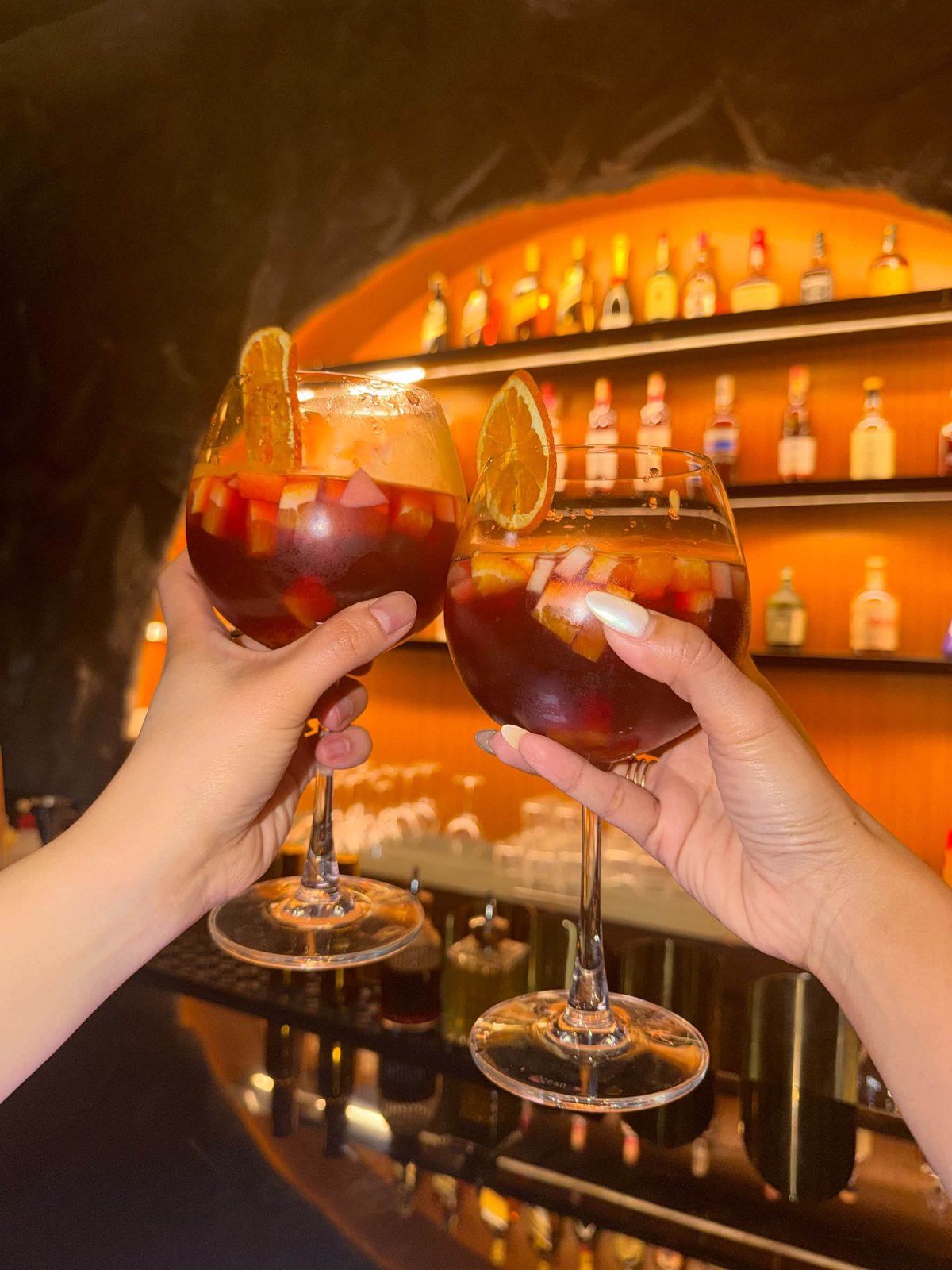 Two glasses of sangria raised in front of the glowing bar arch