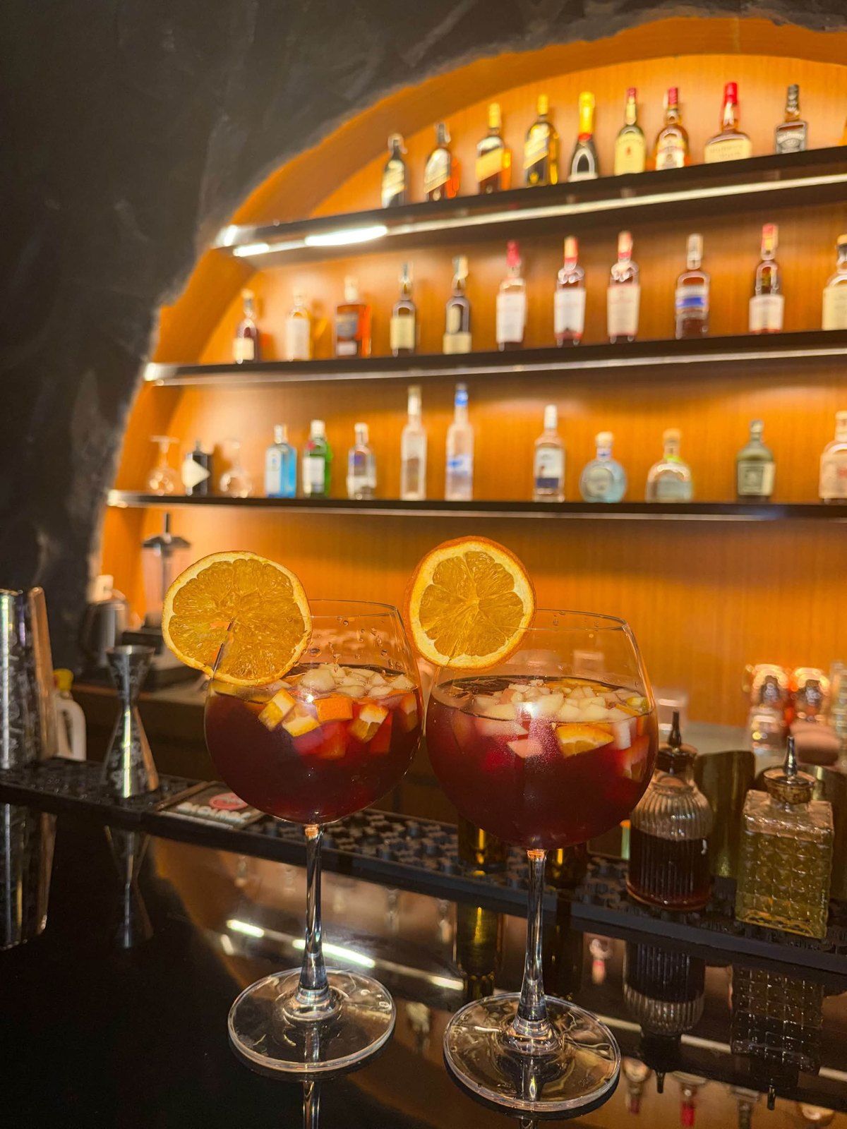 Glasses of sangria with orange slices on the bar under the lit shelves