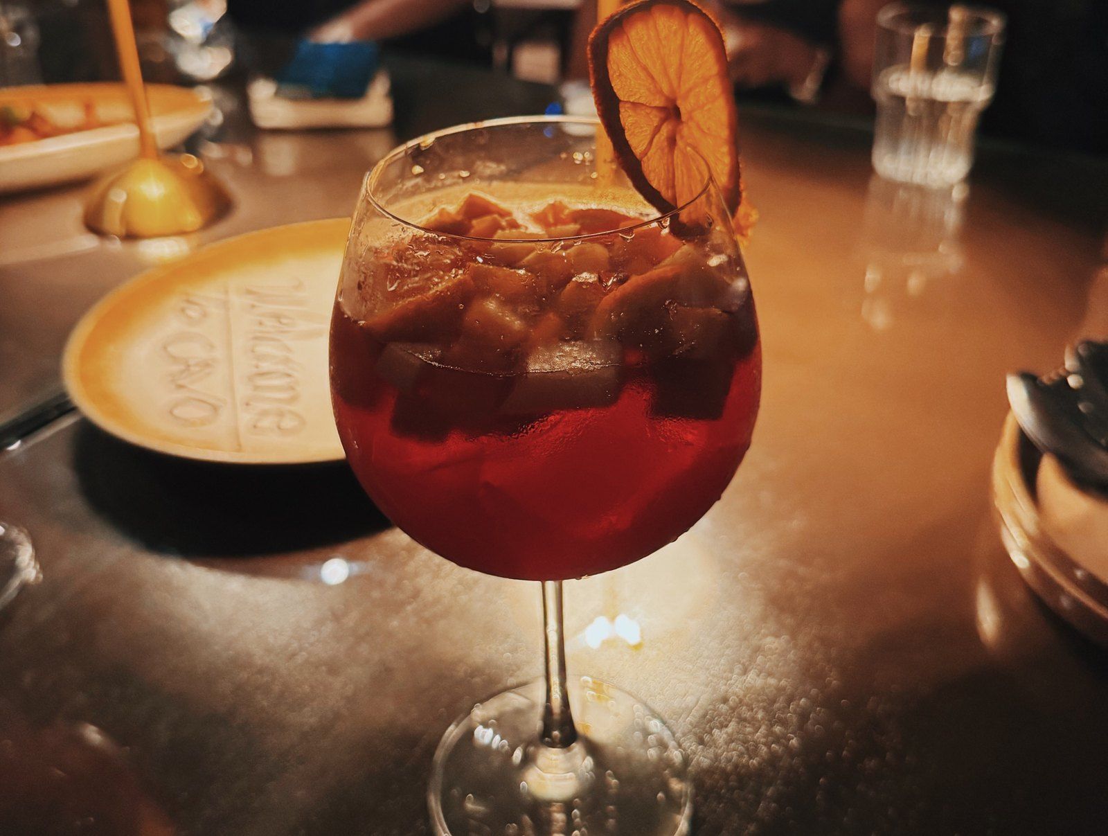 A glass of red sangria with a dried orange slice on a candlelit table