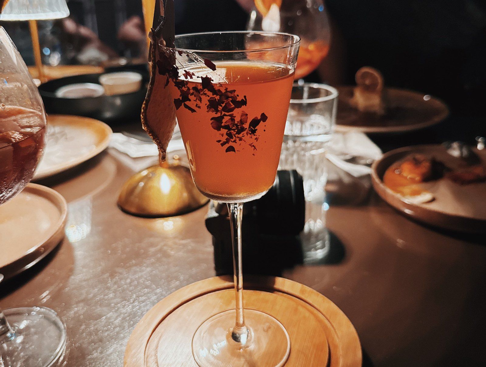 A cocktail in a coupe glass with dried flowers, on a candlelit table