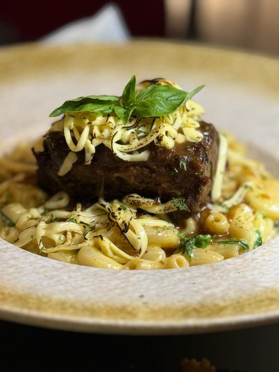 Braised short rib on a bowl of cheesy pasta, topped with crispy strands and basil