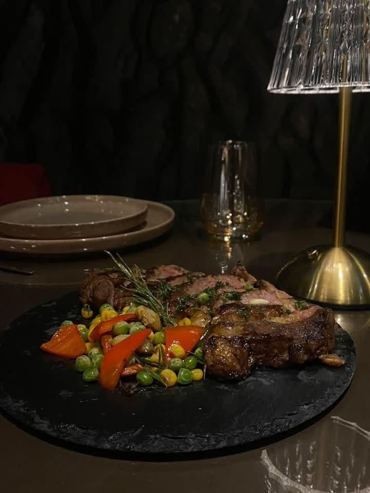 A grilled steak on the bone with sauteed vegetables on a black plate