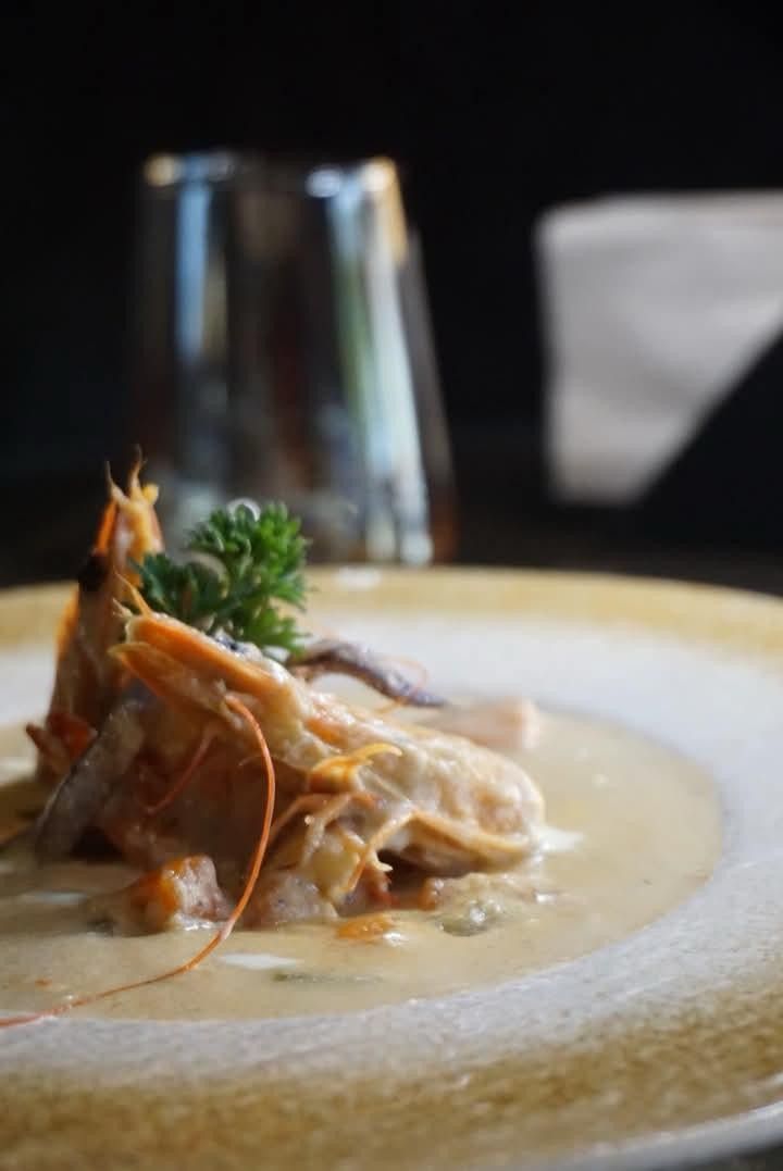A prawn with herbs on a creamy sauce in a white bowl