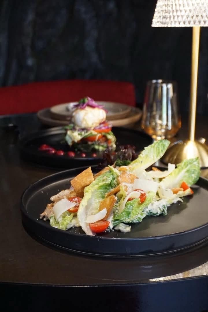 A Caesar salad with romaine and croutons on a black plate