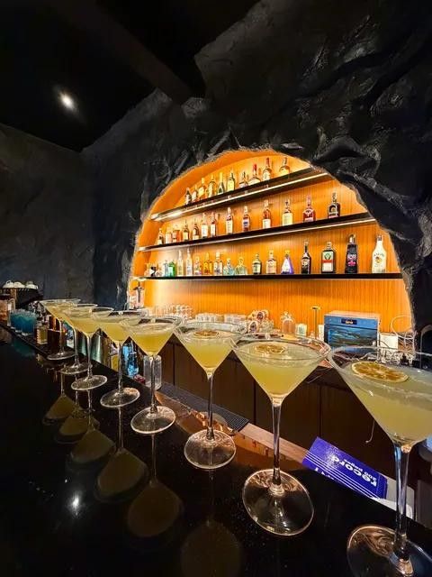 Yellow cocktails in martini glasses lined up along the bar under the glowing arched shelves