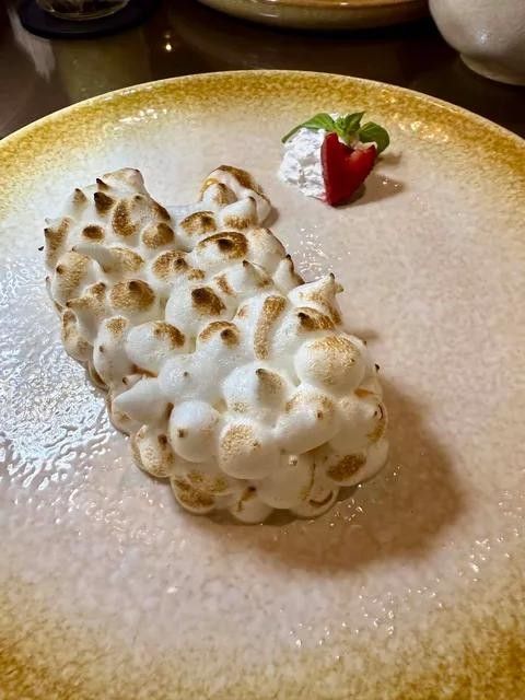 A torched meringue roll with a strawberry on a gold rimmed plate