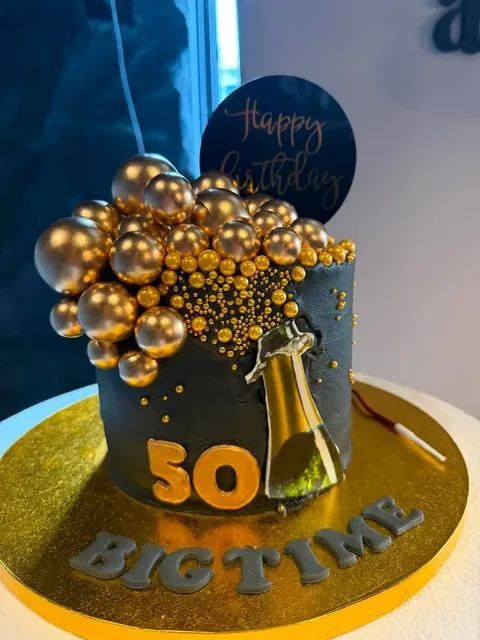 A black and gold birthday cake with gold spheres and a 50 topper