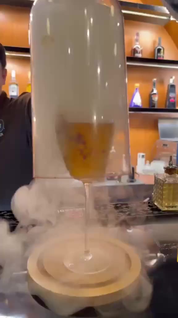 A smoke cloche lifts off an amber cocktail in front of the glowing bar shelves