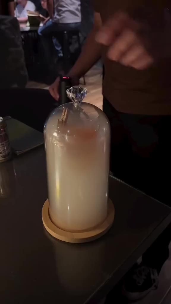 A bartender lifts a smoke filled cloche from a cocktail