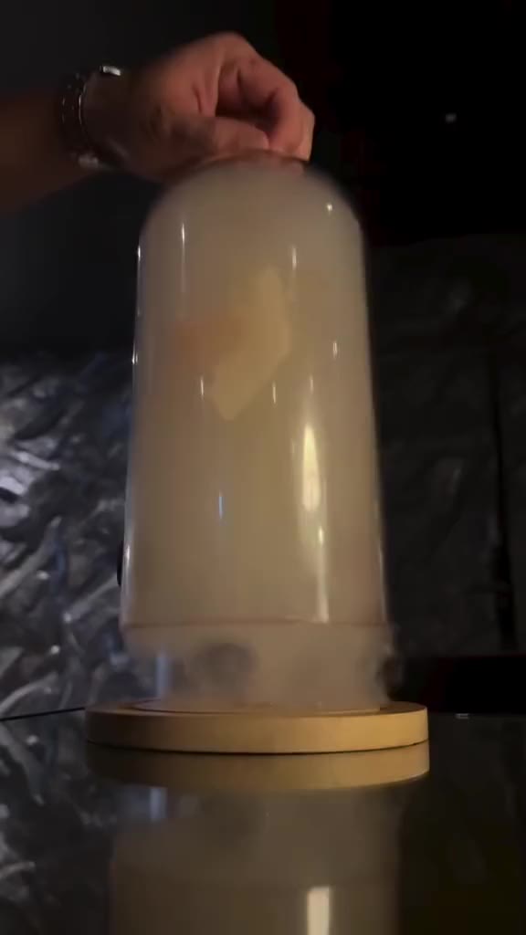 A smoke cloche is lifted from a cocktail on a wooden base