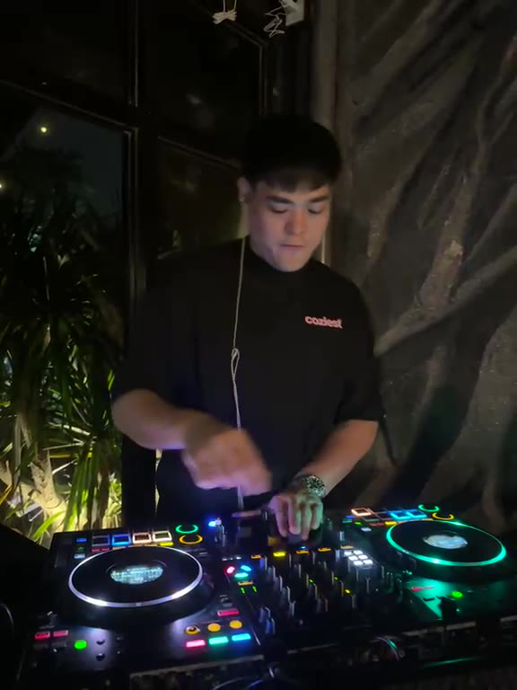 A DJ in a black T shirt mixing on lit decks